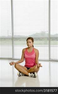 Mid adult Asian woman sitting in yoga lotus position with eyes closed.