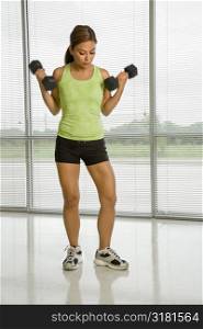 Mid adult Asian woman standing lifting dumbbells.