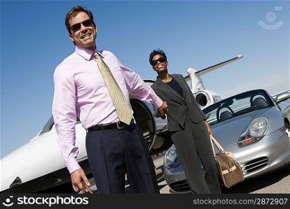 Mid-adult business couple outside of car and airplane.