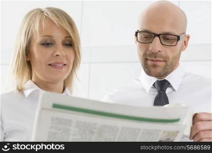 Mid adult business couple reading newspaper in kitchen