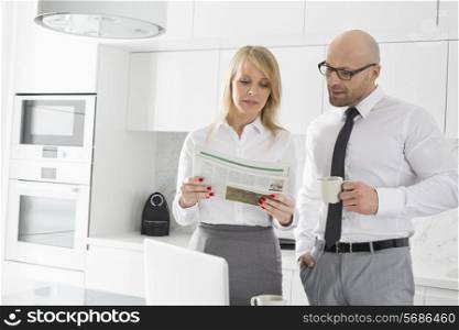 Mid adult business couple reading newspaper while having coffee in kitchen