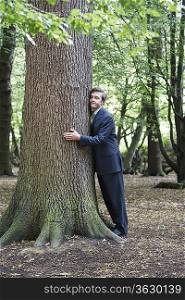 Mid adult business man hugging tree trunk, eyes closed