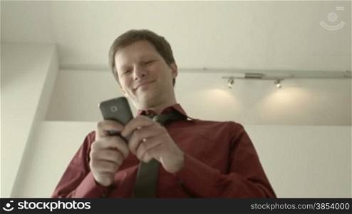 Mid adult business man in office, text messaging on mobile phone. Low angle, dolly shot