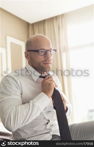 Mid adult businessman adjusting necktie at home