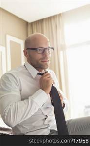 Mid adult businessman adjusting necktie at home