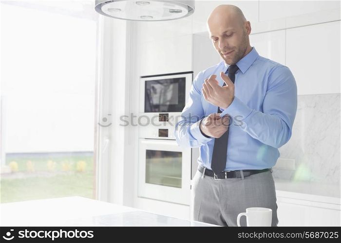 Mid adult businessman buttoning sleeve at home