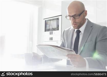 Mid adult businessman having coffee while reading newspaper at home