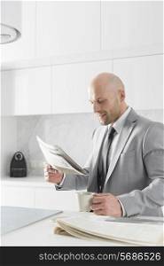 Mid adult businessman having coffee while reading newspaper in kitchen