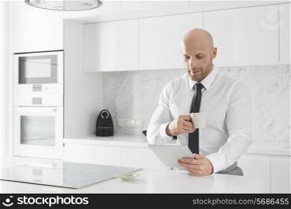 Mid adult businessman having coffee while using tablet PC at kitchen counter