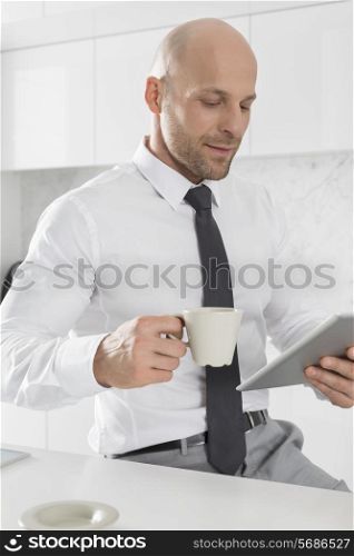 Mid adult businessman having coffee while using tablet PC in kitchen