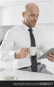 Mid adult businessman having coffee while using tablet PC in kitchen