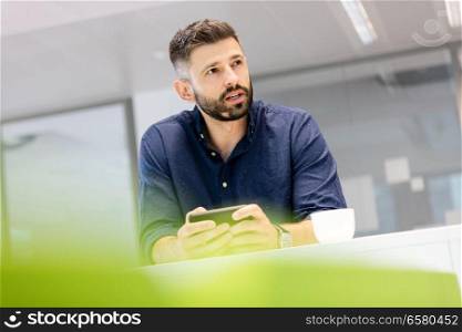 Mid adult businessman holding smartphone while looking away in office