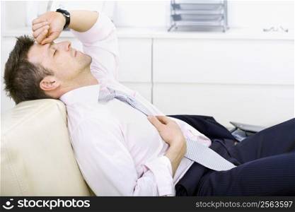 Mid-adult businessman lying on sofa at office, looking tired, eyes closed. Bright background.