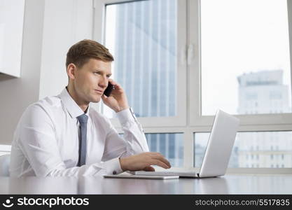 Mid adult businessman on call while using laptop at home