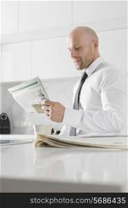 Mid adult businessman reading newspaper at kitchen counter