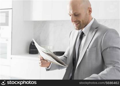Mid adult businessman reading newspaper in kitchen