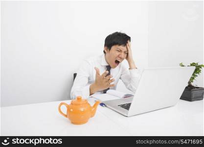 Mid adult businessman screaming with laptop on desk in office