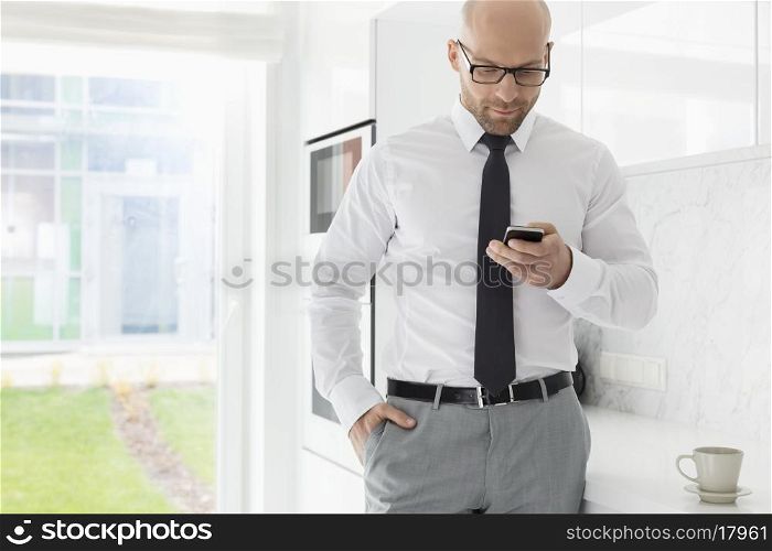 Mid adult businessman text messaging through smart phone at home