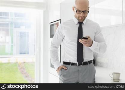 Mid adult businessman text messaging through smart phone at home