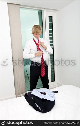 Mid adult businessman tying tie in bedroom