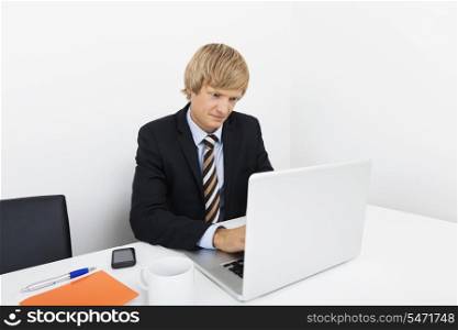 Mid adult businessman using laptop at desk in office