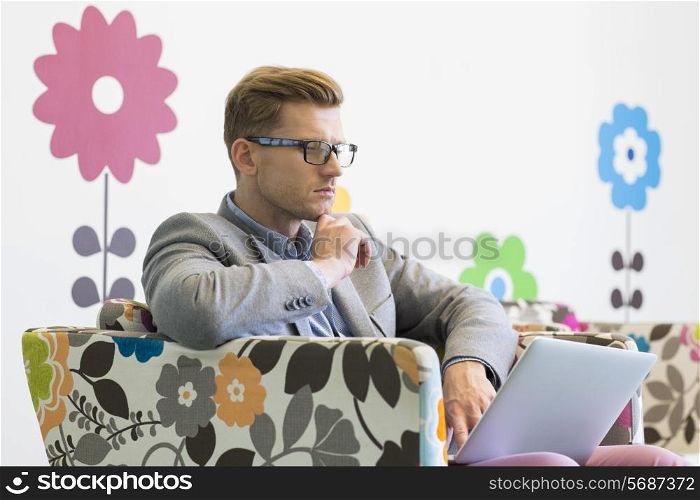 Mid-adult businessman using laptop on armchair in creative office
