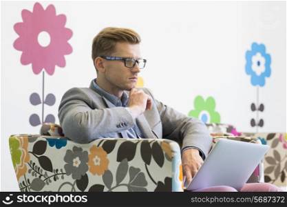 Mid-adult businessman using laptop on armchair in creative office