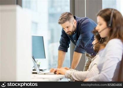 Mid adult businessman using laptop with coworkers wearing headsets in office
