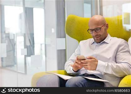 Mid adult businessman using mobile phone while sitting on chair at office