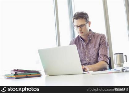 Mid-adult businessman working laptop at desk in creative office