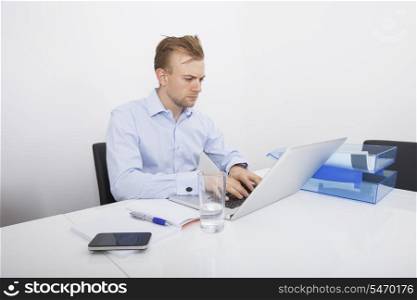 Mid-adult businessman working on laptop at desk in office