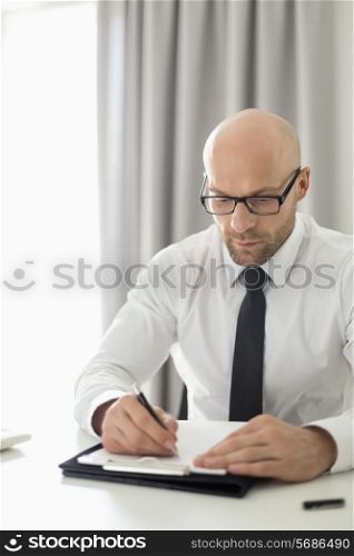 Mid adult businessman writing on clipboard in home office