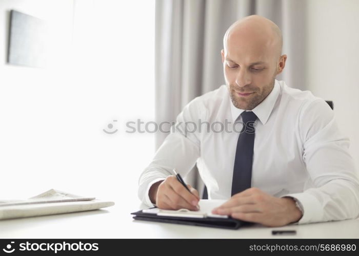 Mid adult businessman writing on clipboard in home office