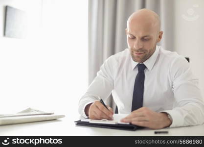 Mid adult businessman writing on clipboard in home office