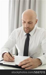 Mid adult businessman writing on clipboard in home office