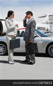 Mid-adult businesswoman and mid-adult businessman standing in front of convertible and talking.