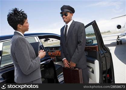 Mid-adult businesswoman and mid-adult chauffeur standing in front of limousine and talking.