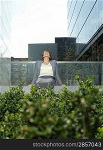 Mid adult businesswoman relaxing on wall outside office buildings