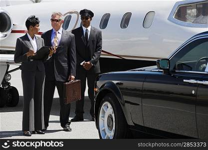 Mid-adult businesswoman, senior businessman and chauffeur in front of private airplane.