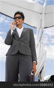 Mid-adult businesswoman using mobile phone in front of airplane.