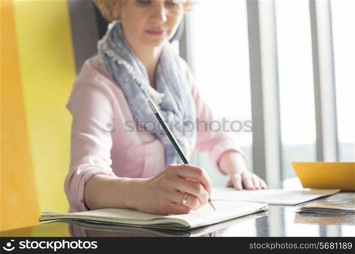 Mid adult businesswoman writing on notepad at desk in office