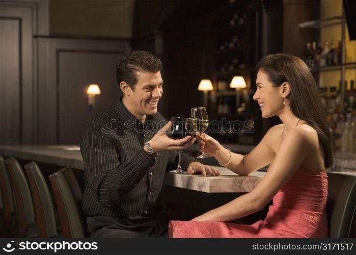 Mid adult Caucasian couple at bar toasting wine glasses and smiling.