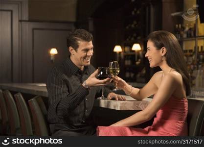 Mid adult Caucasian couple at bar toasting wine glasses and smiling.