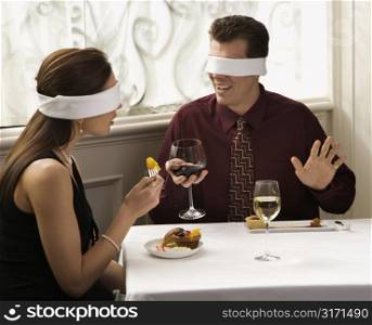 Mid adult Caucasian couple dining in a restaurant with blindfolds over eyes.