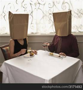 Mid adult Caucasian couple dining in a restaurant with paper bags over heads.