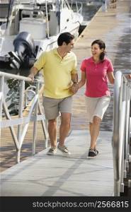 Mid-adult Caucasian couple holding hands and walking up ramp at harbor.