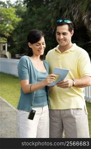 Mid-adult Caucasian couple holding map and smiling.