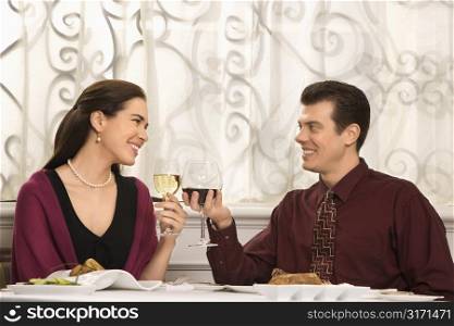 Mid adult Caucasian couple smiling and toasting wine glasses in restaurant.