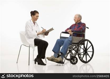 Mid-adult Caucasian female doctor taking notes with an elderly Caucasian male in wheelchair to her side.