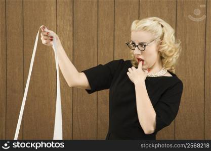 Mid-adult Caucasian female in vintage outfit holding a printout with finger on her lip.